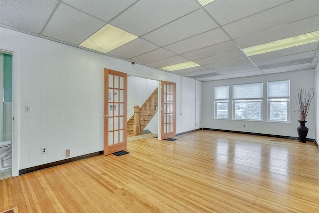 spare room with a drop ceiling, light hardwood / wood-style flooring, and french doors