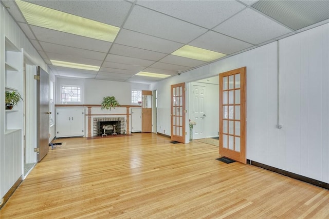 unfurnished living room featuring a fireplace, french doors, light hardwood / wood-style floors, and a drop ceiling