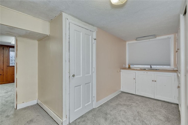 hallway featuring light carpet, sink, and a textured ceiling