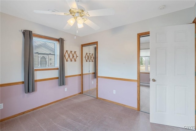 unfurnished bedroom with light carpet, multiple windows, a baseboard heating unit, and ceiling fan