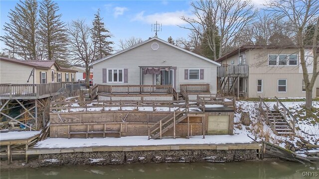 snow covered back of property featuring a deck with water view