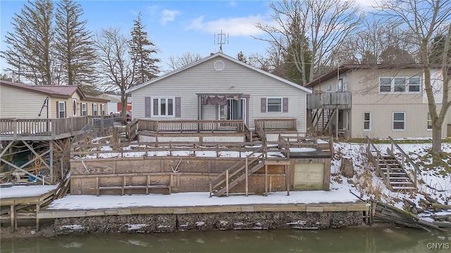 snow covered rear of property with a deck with water view