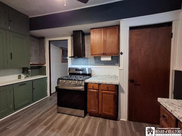 kitchen featuring ceiling fan, stainless steel gas stove, wall chimney range hood, wood-type flooring, and decorative backsplash