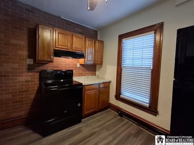 kitchen with black appliances, hardwood / wood-style flooring, ceiling fan, light stone countertops, and brick wall