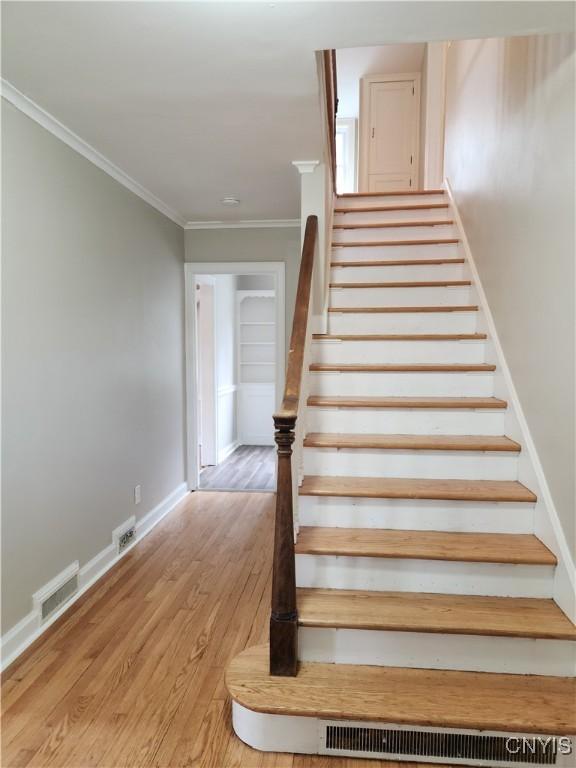 stairs with crown molding and wood-type flooring