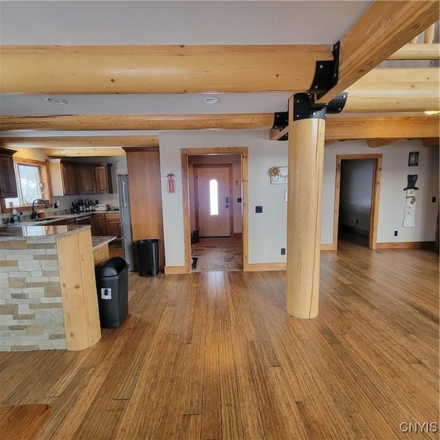 unfurnished living room featuring beamed ceiling, light wood-type flooring, and sink