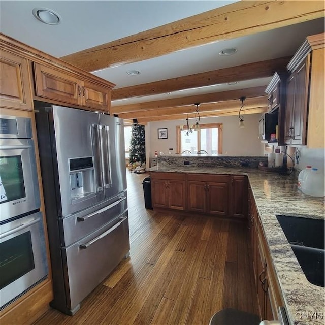 kitchen with beam ceiling, light stone countertops, hanging light fixtures, dark hardwood / wood-style flooring, and appliances with stainless steel finishes