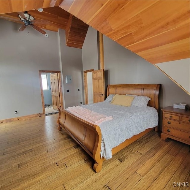 bedroom featuring light wood-type flooring, ensuite bathroom, ceiling fan, wooden ceiling, and vaulted ceiling with beams