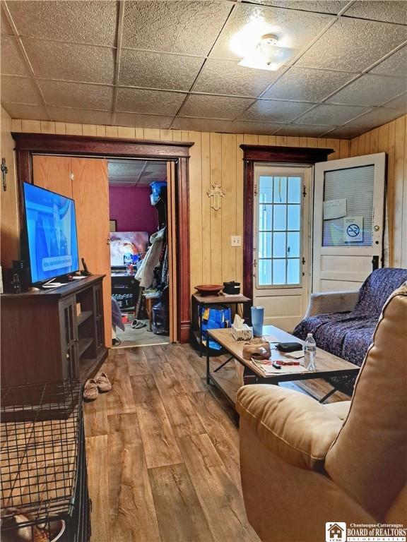 living room with a paneled ceiling, wood walls, and wood-type flooring