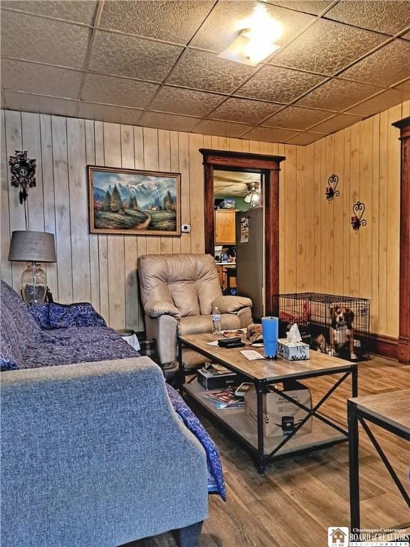 living room with wood walls, a drop ceiling, and hardwood / wood-style flooring