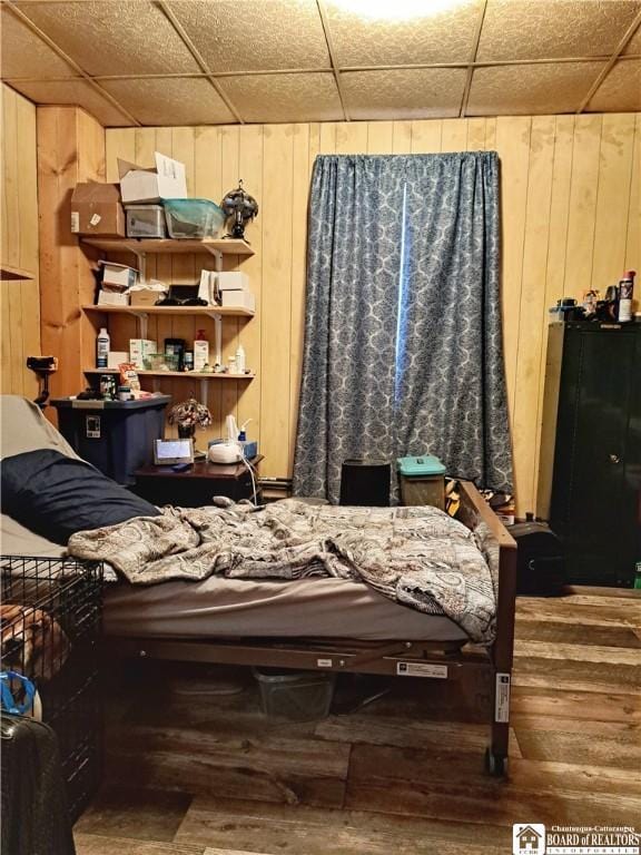 bedroom featuring a paneled ceiling, hardwood / wood-style floors, and wooden walls