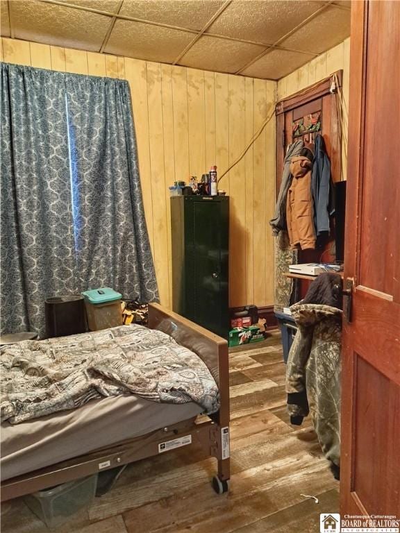 bedroom with hardwood / wood-style flooring, a drop ceiling, and wooden walls