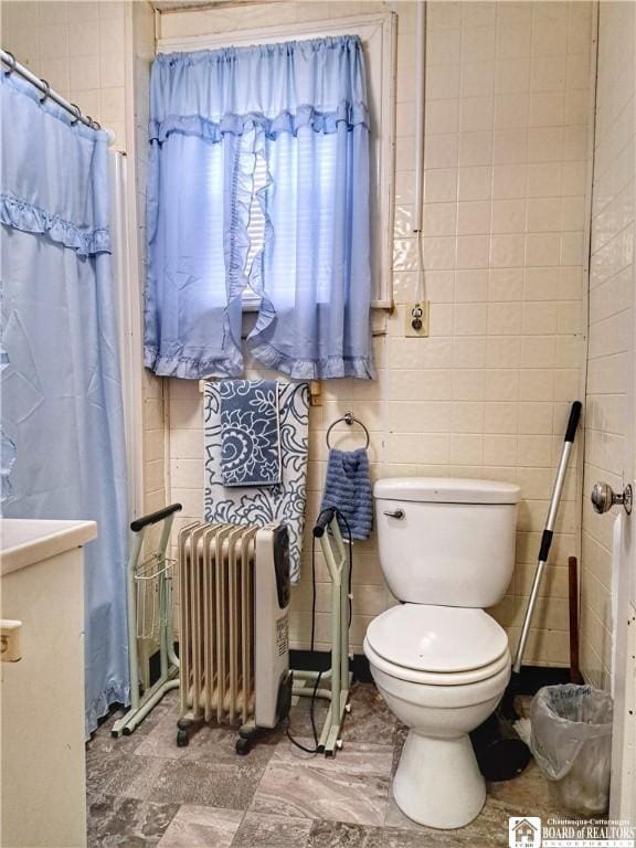 bathroom with vanity, radiator, a shower with shower curtain, toilet, and tile walls