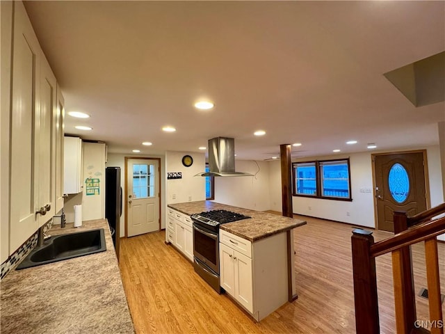 kitchen featuring gas range, sink, island exhaust hood, light hardwood / wood-style floors, and white cabinets