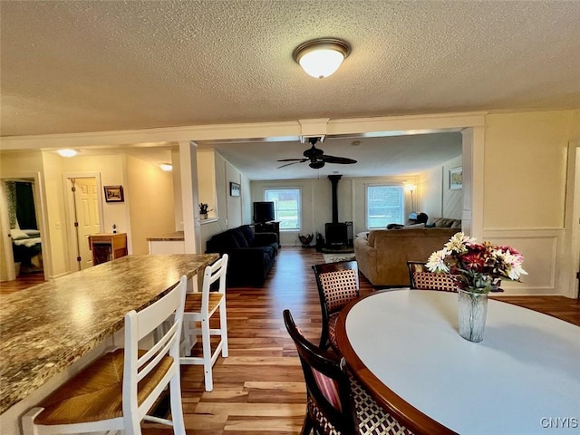 dining room with wood-type flooring, a textured ceiling, a wood stove, and ceiling fan