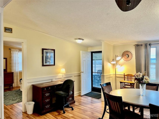 dining room with vaulted ceiling, crown molding, light hardwood / wood-style floors, and a textured ceiling