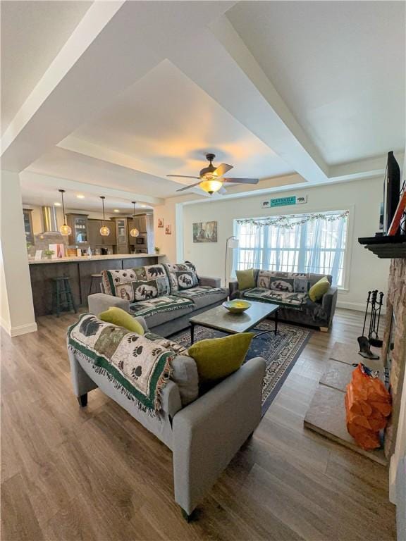 living room featuring a raised ceiling, a stone fireplace, ceiling fan, and hardwood / wood-style floors