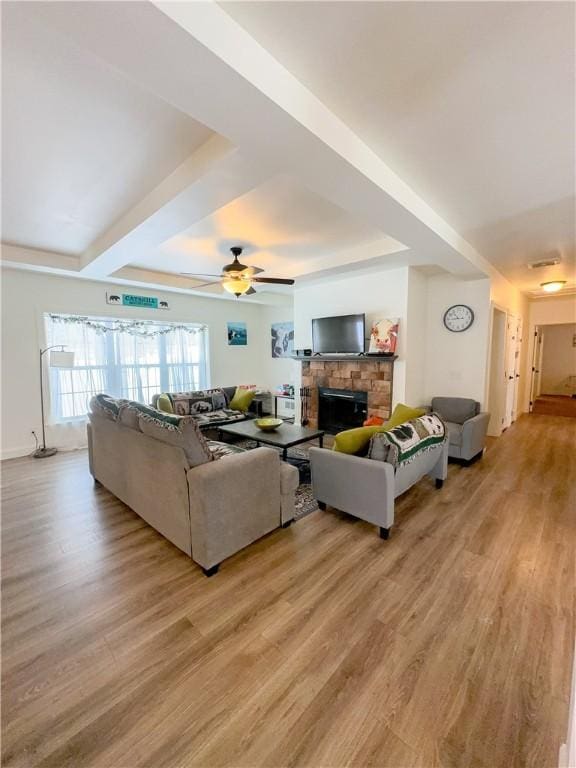 living room with a stone fireplace, ceiling fan, and light wood-type flooring