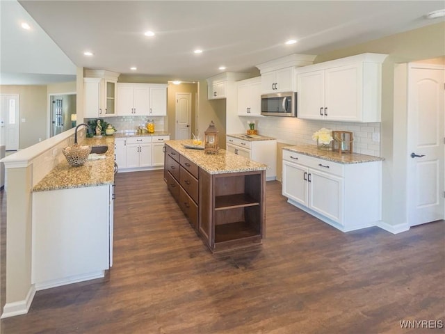 kitchen with kitchen peninsula, decorative backsplash, dark hardwood / wood-style flooring, sink, and white cabinetry