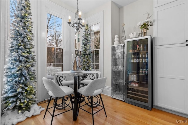 dining room featuring bar, wine cooler, a chandelier, and light hardwood / wood-style floors