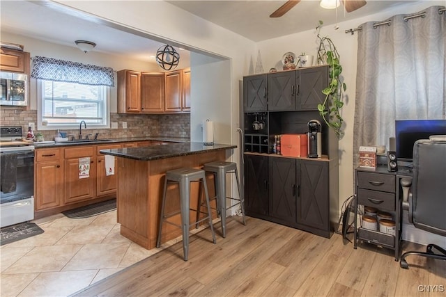 kitchen featuring a breakfast bar, sink, tasteful backsplash, white electric stove, and kitchen peninsula