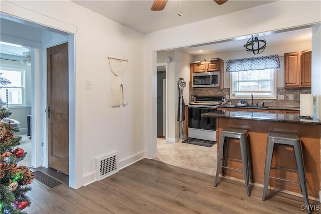 kitchen with a breakfast bar, pendant lighting, white electric range, backsplash, and ceiling fan