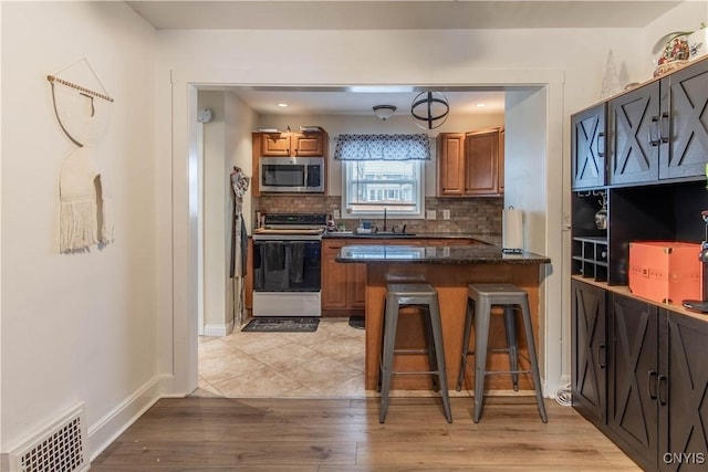 kitchen featuring sink, a breakfast bar area, electric range, decorative backsplash, and kitchen peninsula