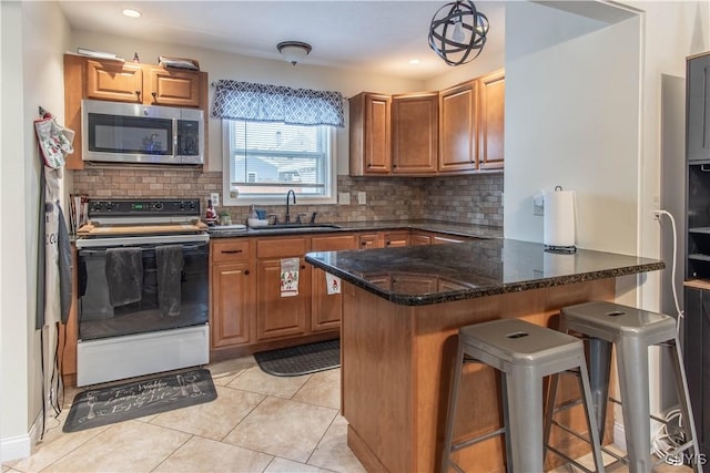 kitchen with sink, a kitchen breakfast bar, white range with electric stovetop, decorative light fixtures, and dark stone counters