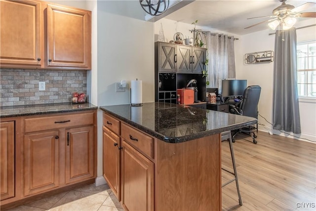 kitchen with ceiling fan, tasteful backsplash, light hardwood / wood-style floors, a kitchen bar, and kitchen peninsula