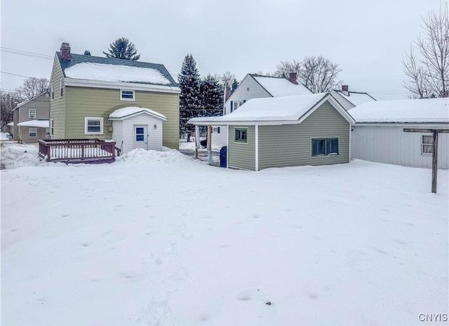 snow covered rear of property with a wooden deck and an outbuilding