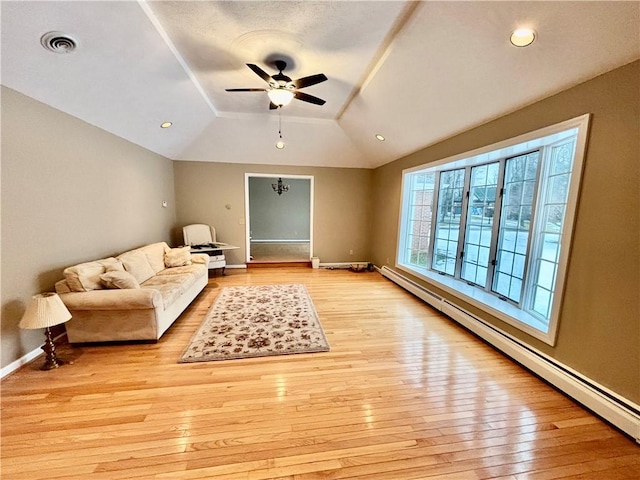 living area with a baseboard heating unit, visible vents, vaulted ceiling, and light wood-style floors