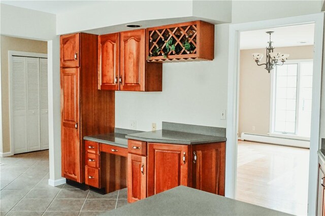 kitchen with light tile patterned floors, a baseboard heating unit, hanging light fixtures, brown cabinets, and dark countertops