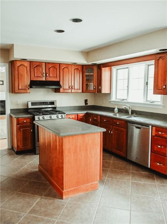 kitchen with a center island, stainless steel appliances, dark countertops, a sink, and under cabinet range hood