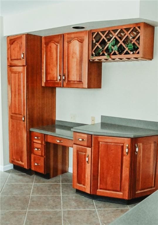 kitchen featuring light tile patterned floors, built in desk, dark countertops, and brown cabinets