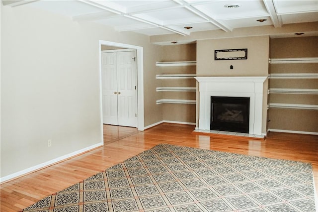 unfurnished living room with built in features, a fireplace with flush hearth, light wood-type flooring, coffered ceiling, and baseboards