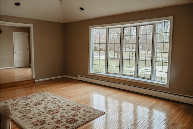 empty room featuring lofted ceiling, baseboard heating, wood-type flooring, and baseboards