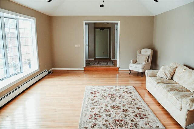 living area featuring vaulted ceiling, baseboard heating, baseboards, and light wood-style floors