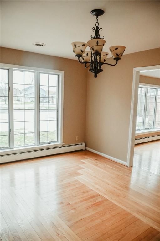 unfurnished dining area featuring baseboards, light wood-style floors, a baseboard radiator, and a notable chandelier