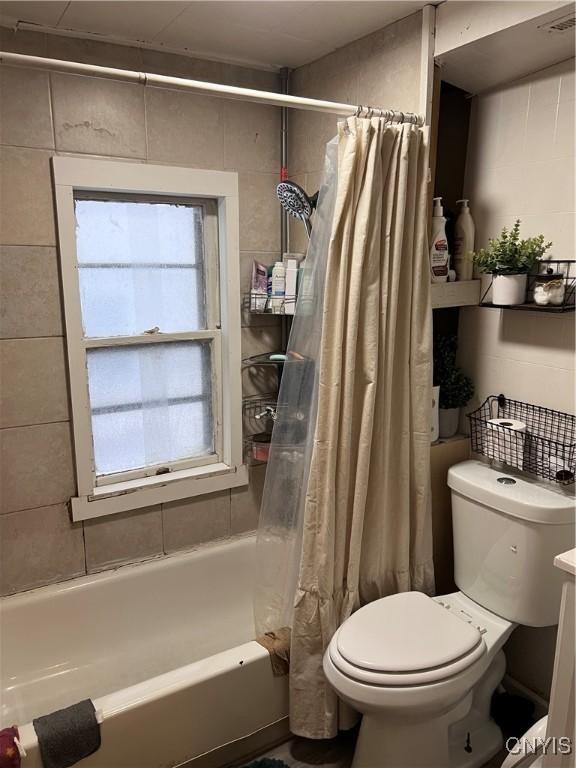 bathroom with toilet, tile walls, and shower / bath combo with shower curtain