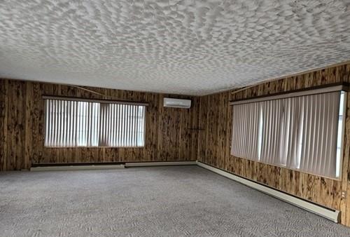 spare room featuring baseboard heating, a wall mounted AC, wooden walls, and carpet