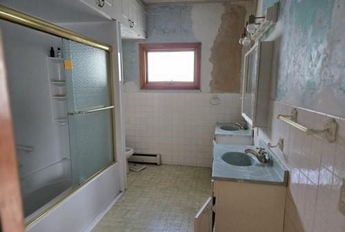 full bathroom with vanity, a baseboard heating unit, toilet, enclosed tub / shower combo, and tile walls