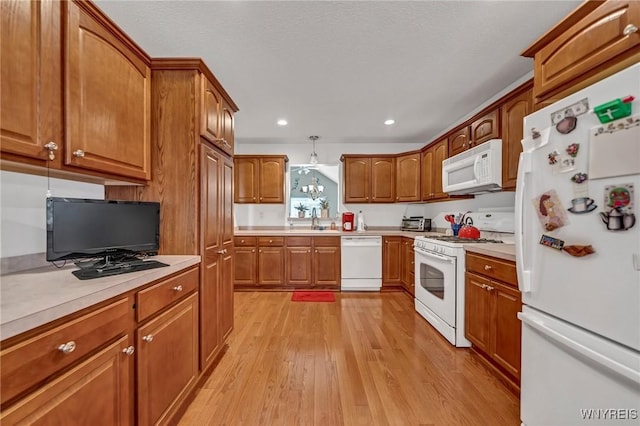 kitchen with sink, hanging light fixtures, white appliances, and light hardwood / wood-style floors