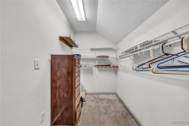 walk in closet with light colored carpet and vaulted ceiling