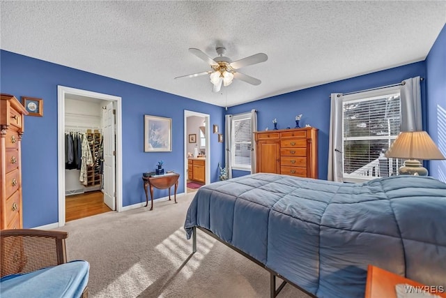 carpeted bedroom featuring ensuite bath, ceiling fan, a textured ceiling, a walk in closet, and a closet