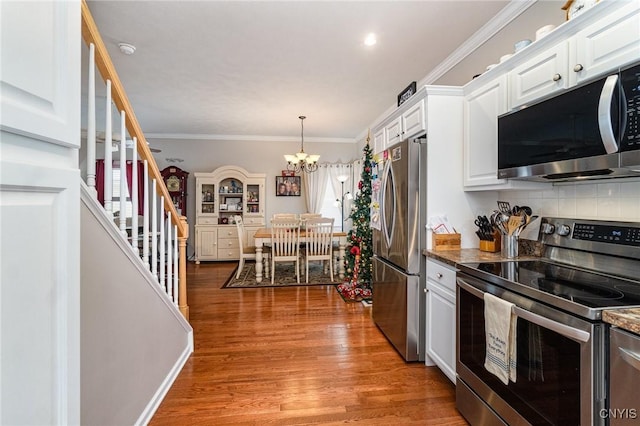 kitchen with dark stone counters, an inviting chandelier, white cabinets, crown molding, and appliances with stainless steel finishes