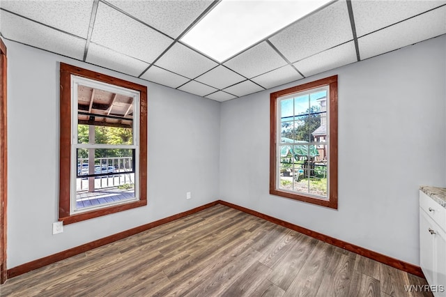 empty room featuring wood-type flooring, a paneled ceiling, and plenty of natural light