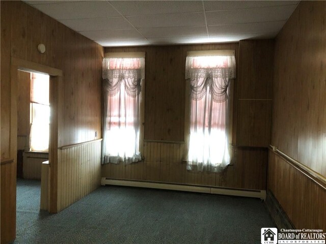 spare room featuring baseboard heating, wooden walls, and dark colored carpet