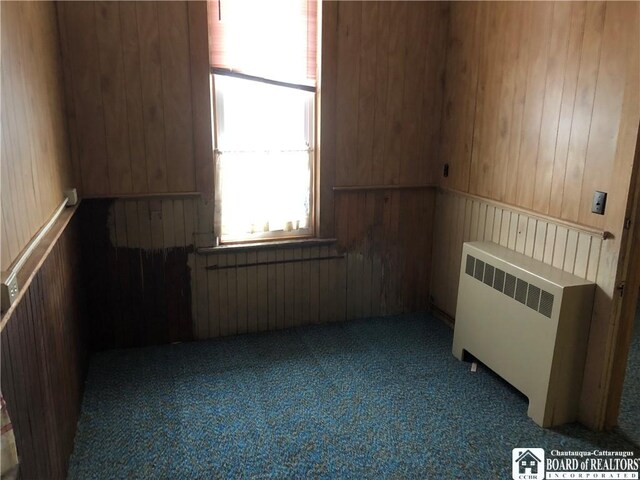 carpeted empty room featuring radiator heating unit and wooden walls