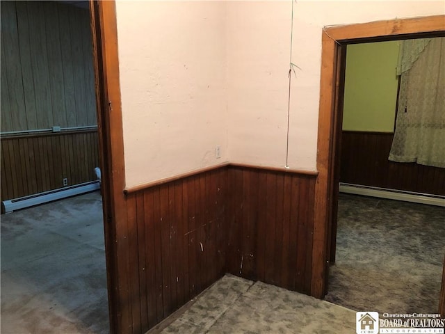 carpeted spare room featuring wood walls and a baseboard heating unit