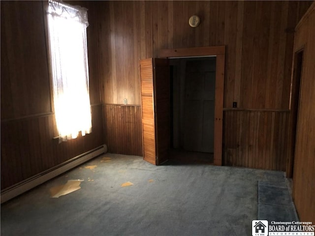 carpeted spare room with baseboard heating and wooden walls